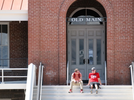 Two people sitting on the steps of Old Main.