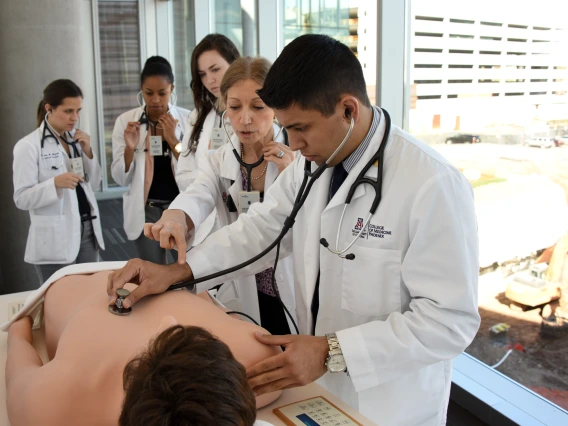 A person wearing a lab coat and stethoscope practicing on a dummy. 