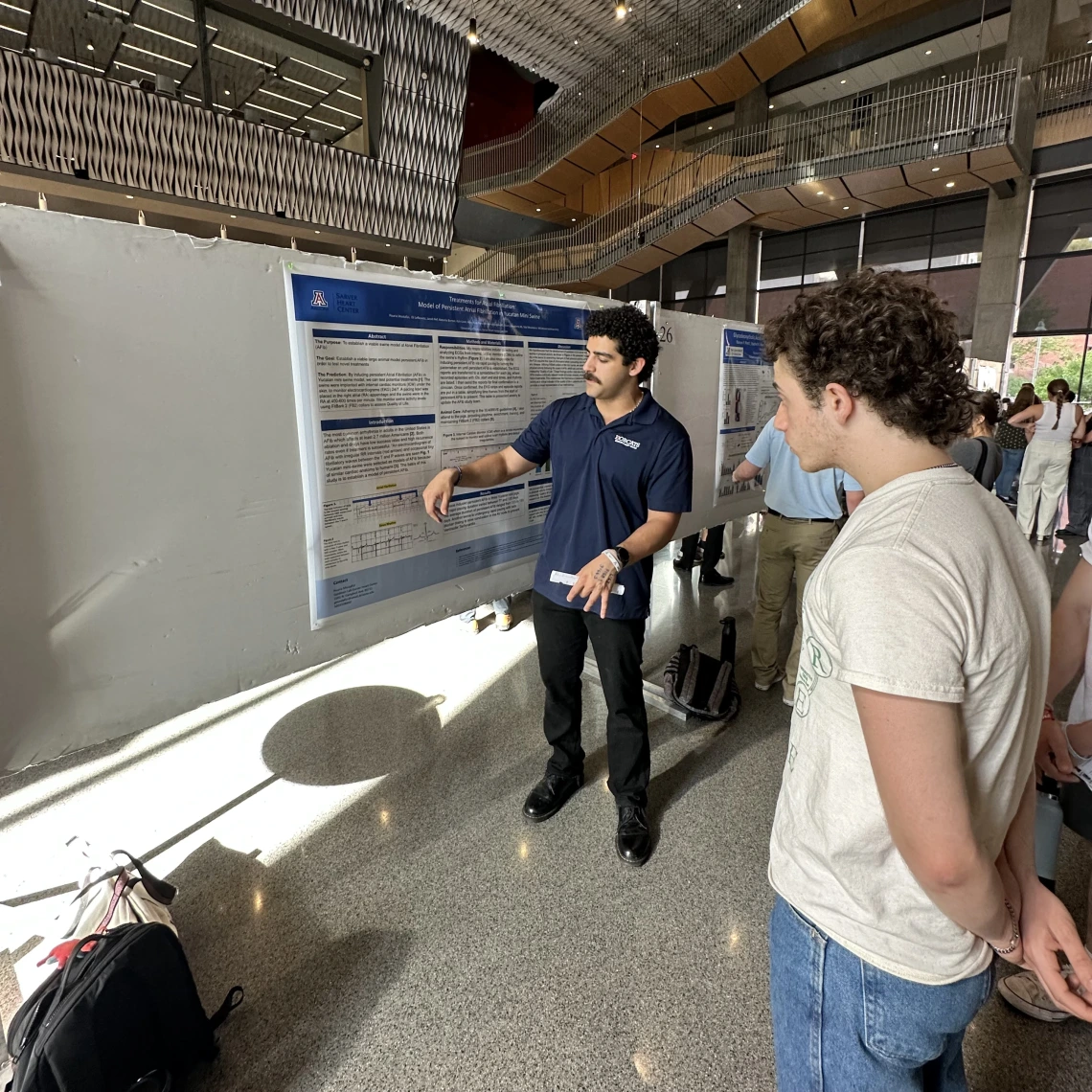 A person wearing a UA polo standing in front of a poster presenting their research.