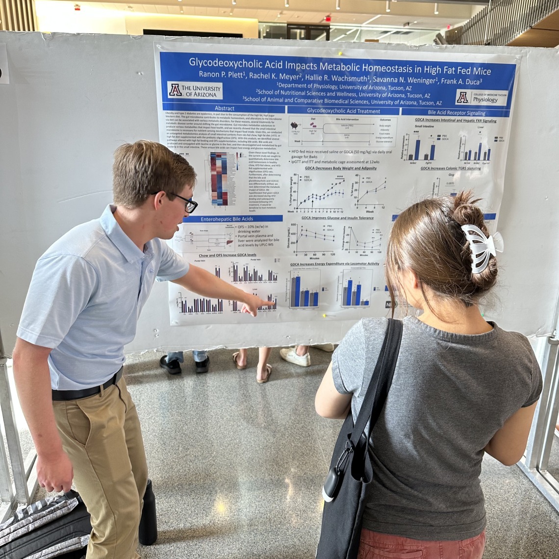 A person pointing at a poster explaining their research to another person.