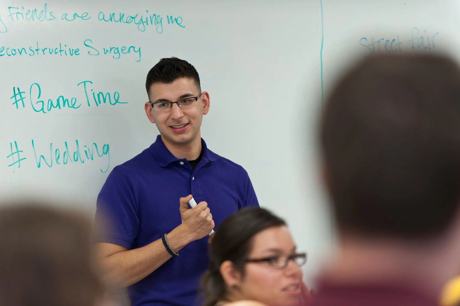 A person with glasses standing in front of a whiteboard with a whiteboard marker.